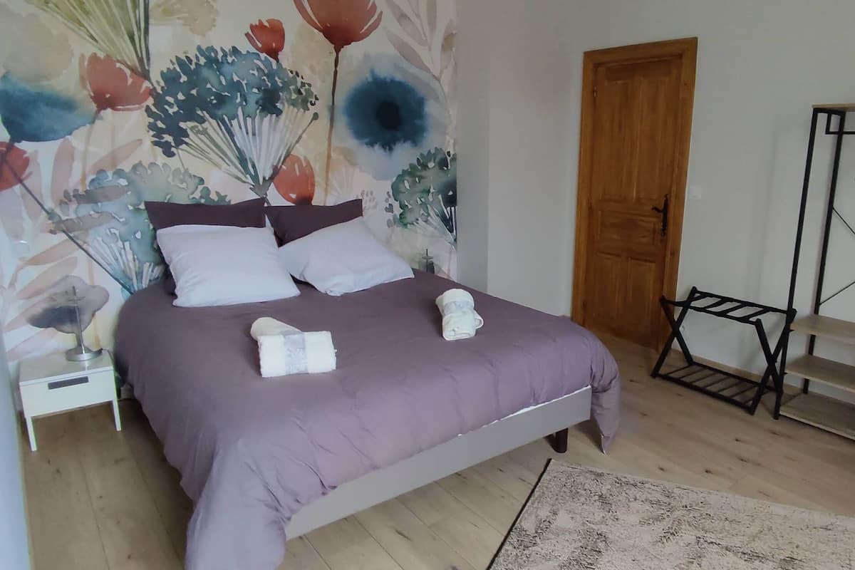 Ein Schlafzimmer mit einem Bett, einem Nachttisch, einer Holztür, einem Metallregal und einer Wand mit Blumenmuster.