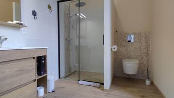 A bathroom with a glass-enclosed shower, a toilet, and a sink with a wooden vanity.