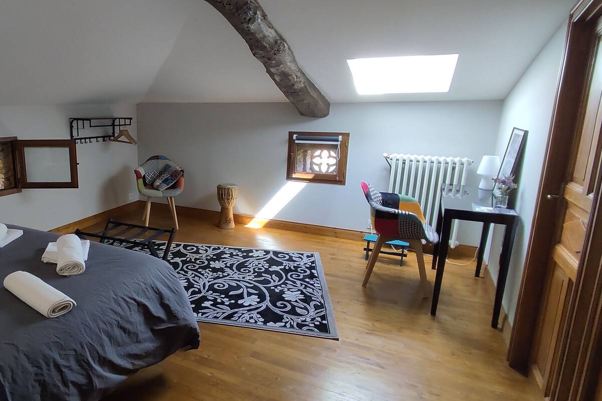 Ein Schlafzimmer mit einem großen Bett, einem kleinen Tisch, einem Stuhl, einem Fenster und einer Heizung.
