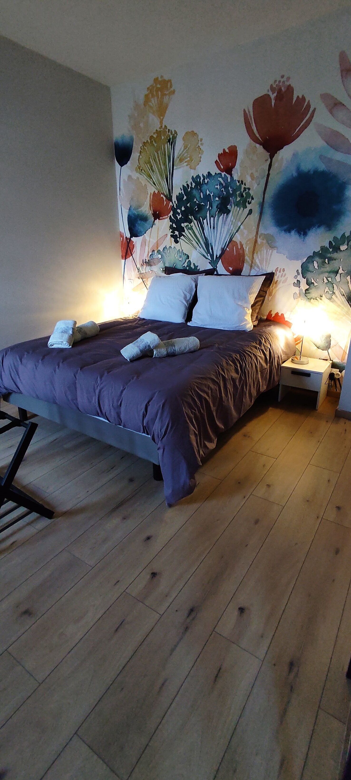 A bedroom with a bed, wooden flooring, and a wall mural.