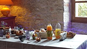 A breakfast buffet with various food items and drinks on a table in a room with stone walls and a window.