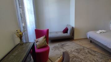 A bedroom with a bed, a red chair, a grey sofa, and a wooden table.