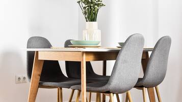 A dining table with four grey upholstered chairs, a white vase with flowers, and a green bowl.