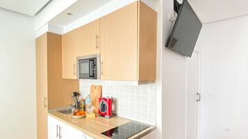Cocina compacta con armarios de madera, microondas, lavamanos y placa de inducción integrada.
