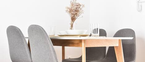 Una mesa de comedor con cuatro sillas grises tapizadas, un cuenco blanco y un florero con flores secas.