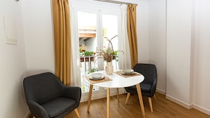 A dining area with two chairs, a round table, and a view of a balcony with plants and a wooden structure.