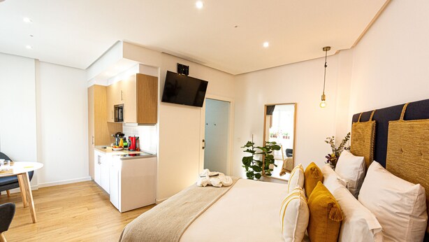 A modern bedroom with a large bed, bedside tables, a TV, and a kitchenette.