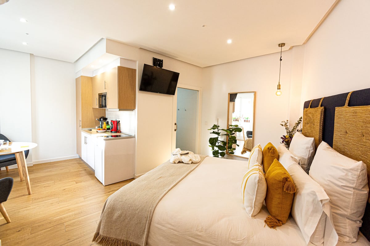 Een moderne slaapkamer met een groot bed, nachtkastjes, een televisie en een kitchenette.