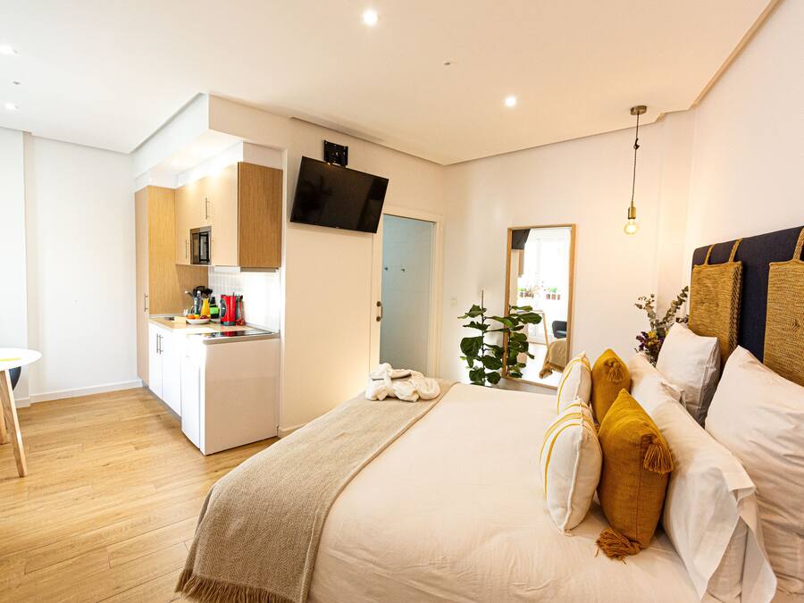 Un dormitorio moderno con una cama grande, mesitas de noche, televisión y kitchenette.