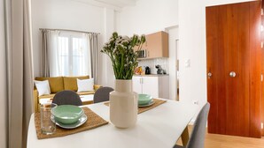 A modern dining area with a white table, green bowls, and a vase of flowers.