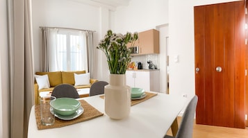 A modern dining area with a white table, green bowls, and a vase of flowers.