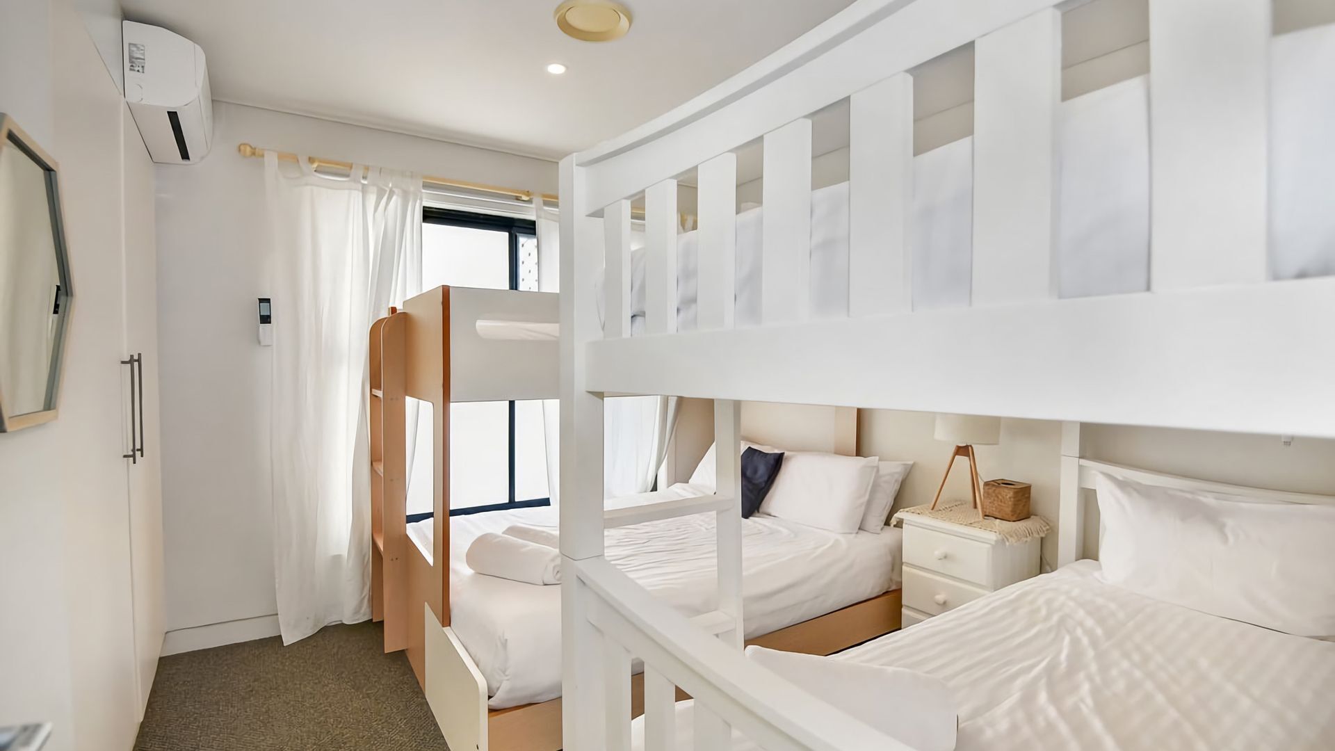 Une chambre avec un lit superposé, une fenêtre, une table de chevet et un appareil de climatisation.