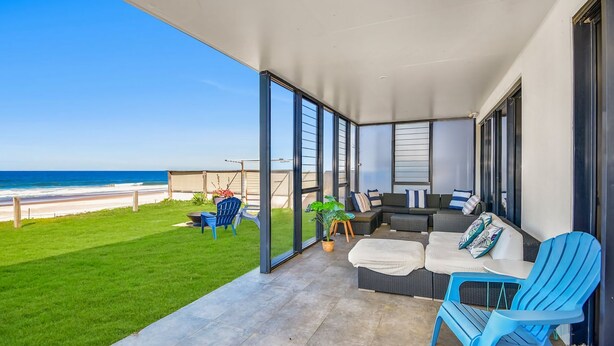 A balcony with a view of the beach, a sofa, a chair, and a small table. - Beach Bliss The Entrance North (The Entrance North)