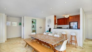 A modern kitchen with wooden cabinets, a built-in refrigerator, and a dining area with a wooden table and white chairs. - Beach Bliss The Entrance North (The Entrance North)