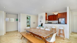 A modern kitchen with wooden cabinets, a built-in refrigerator, and a dining area with a wooden table and white chairs.