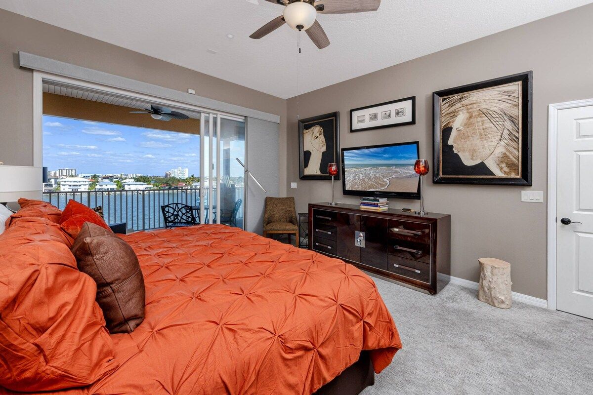 A bedroom with a large bed, a television, artwork on the wall, and a view through a sliding door.