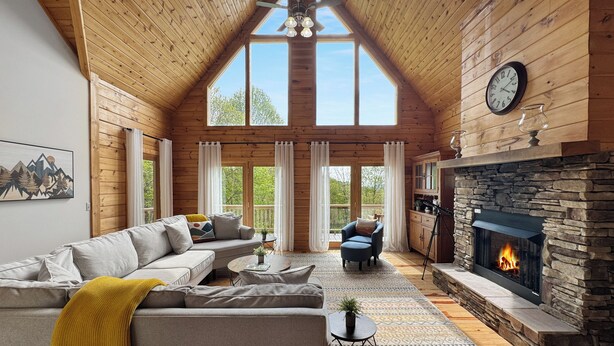 Accogliente interno di una baita in legno con camino in pietra, soffitto in legno e ampie finestre.