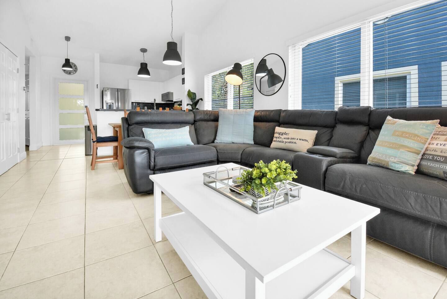 Ein modernes Wohnzimmer mit einem Ecksofa, einem weißen Couchtisch und einer Küche im Hintergrund.