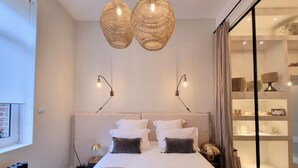 Un dormitorio con una cama grande, dos lámparas de pared, un ventanal y una puerta de cristal que da al baño.