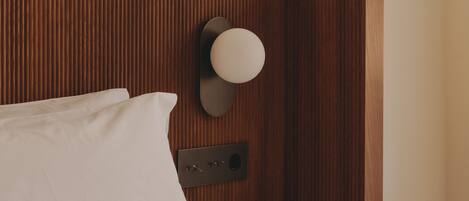 A neatly made bed with white linens, a bedside table with a glass of water, and a wall-mounted light fixture.