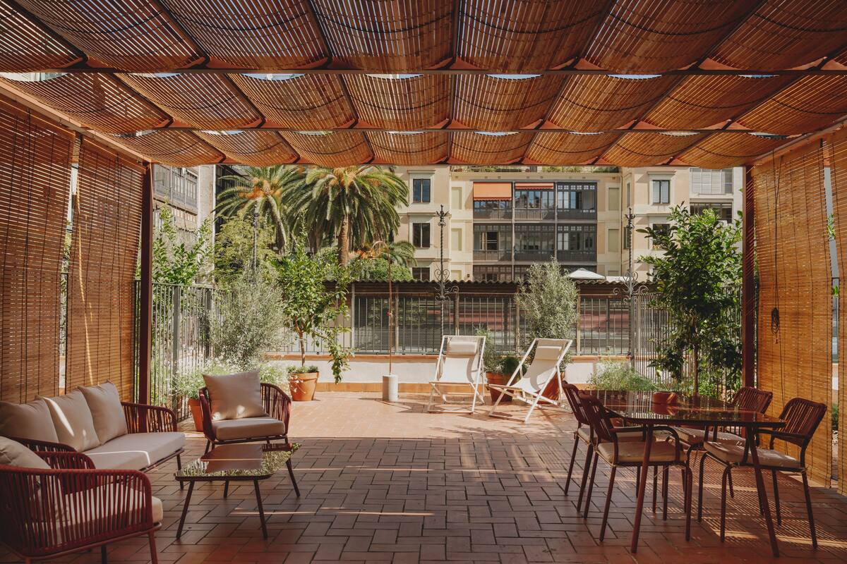 An outdoor patio with wicker furniture, a brick floor, and a view of buildings and trees.