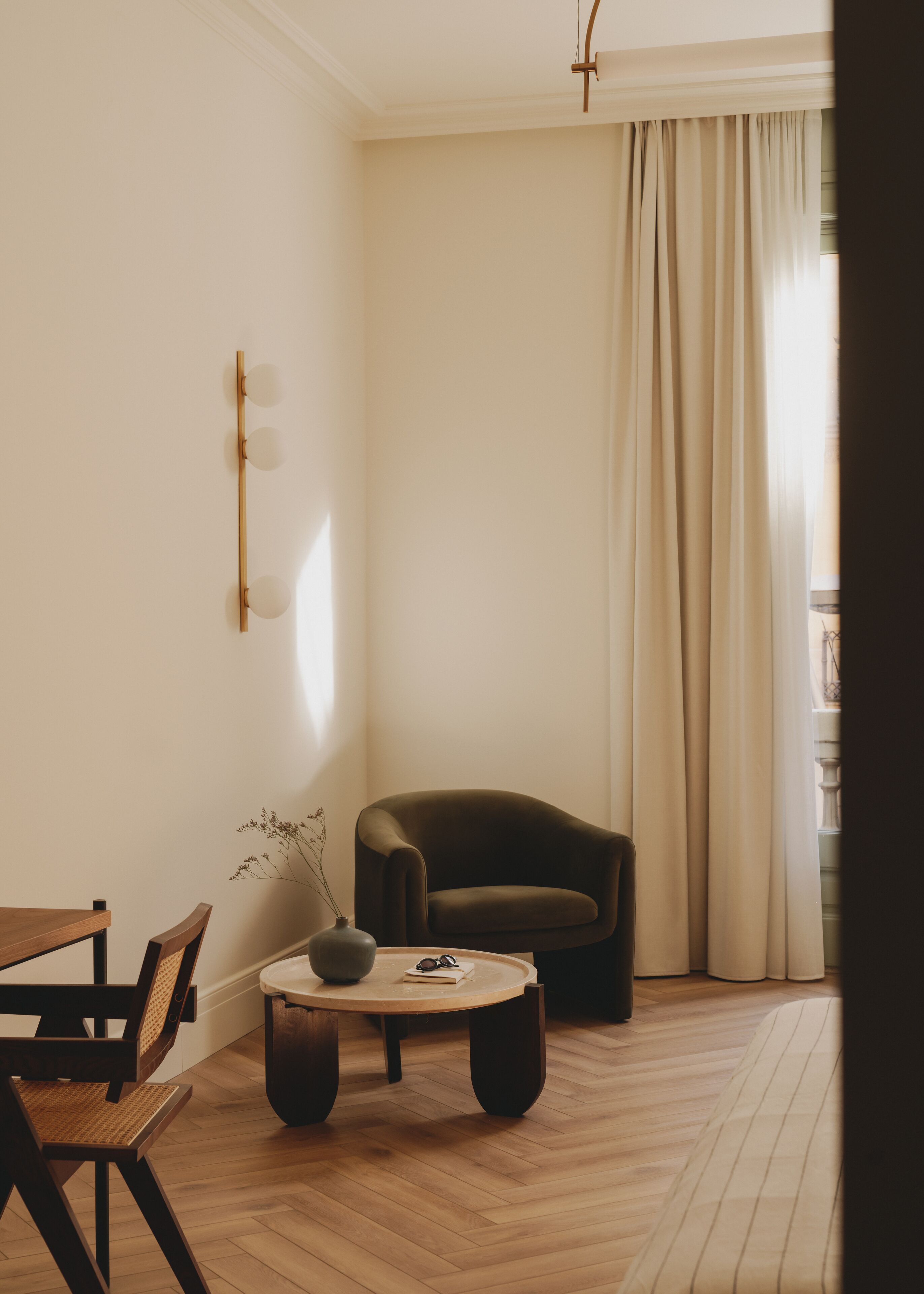 A minimalist living room with a wooden floor, a dark brown armchair, a round coffee table, and a dining area with a wooden table and chairs.