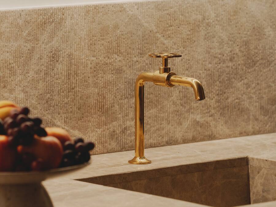 A bathroom with a gold faucet and a bowl of fruit on the counter.