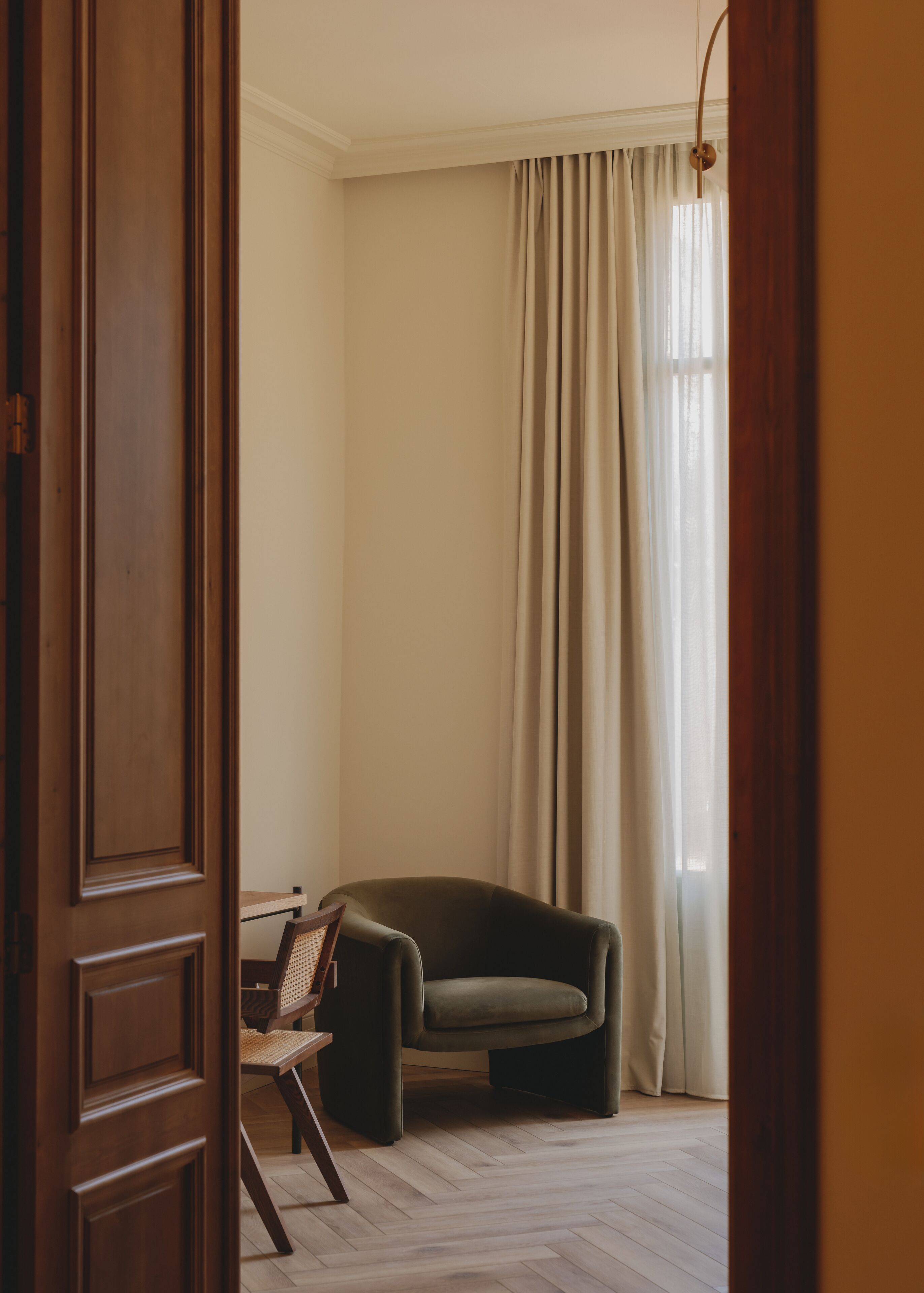 A room with a wooden door, a chair, a table, and a window with curtains.