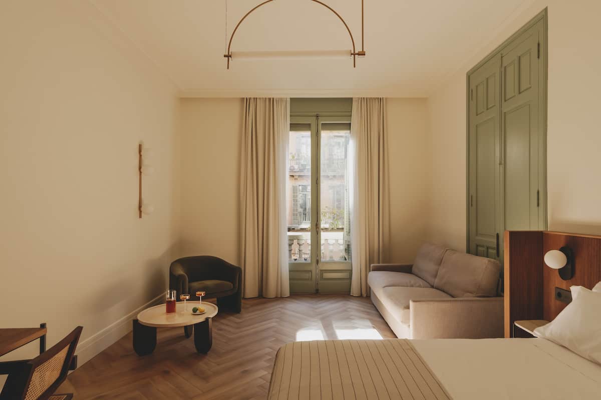 A hotel room with a bed, a sofa, a chair, a small table, and a window with curtains.