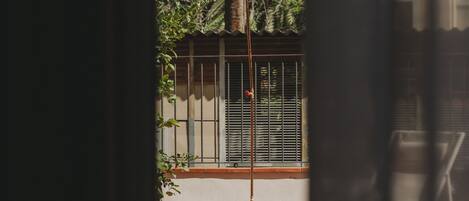A view through a window with a metal gate, a concrete pillar, and a tiled patio area.