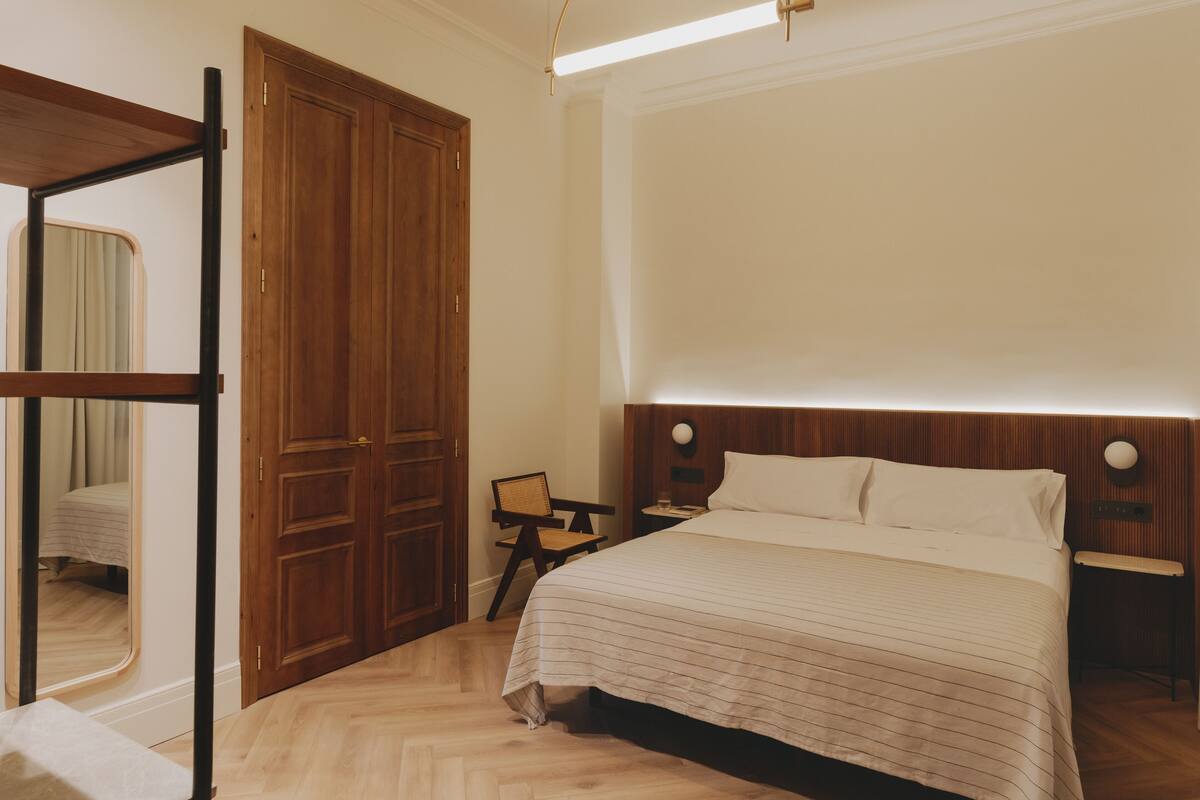 A hotel room with a large bed, wooden wardrobe, and a small table with a chair.