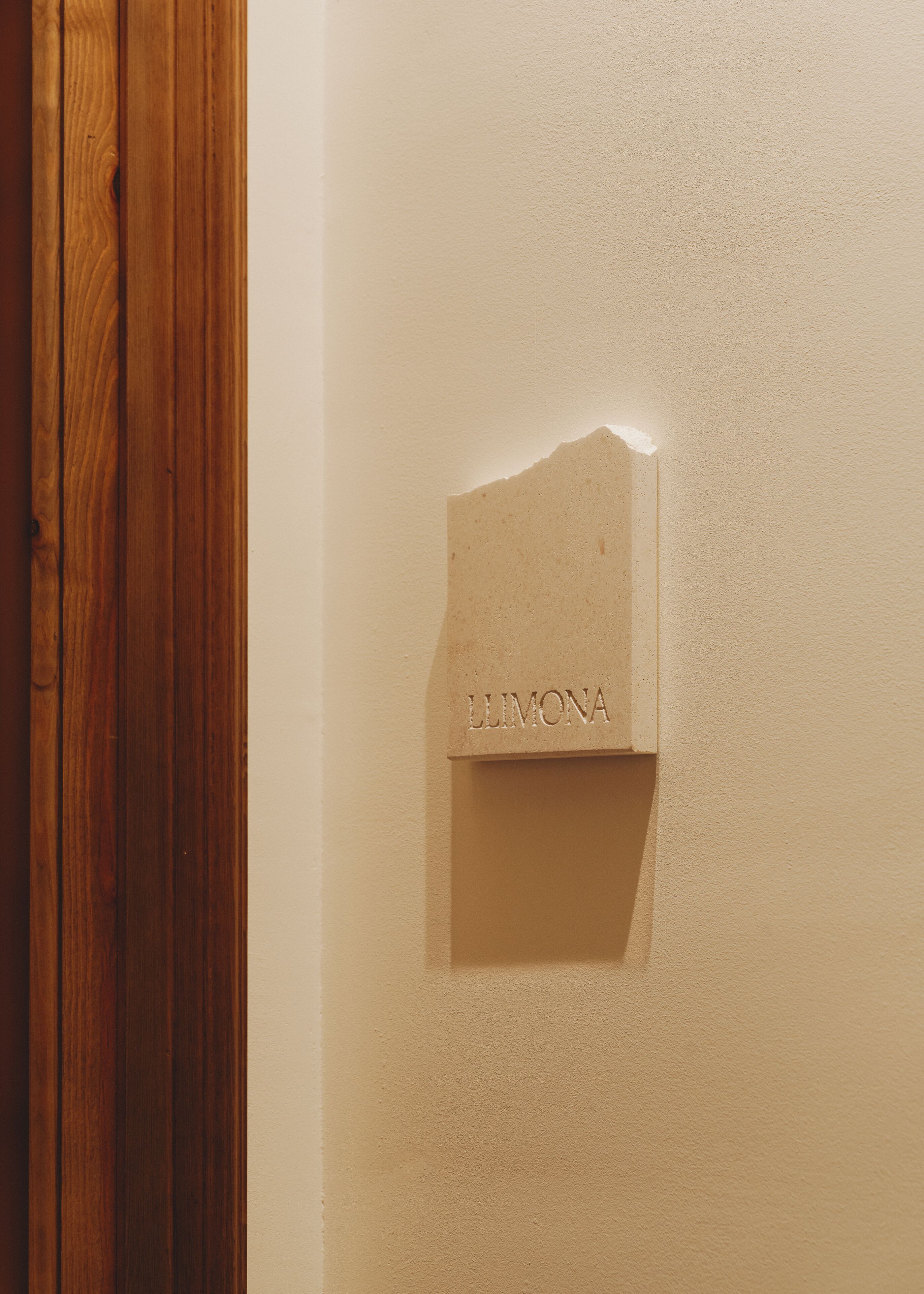 A wooden door adjacent to a wall with a recessed plaque labeled "LLIMONA".