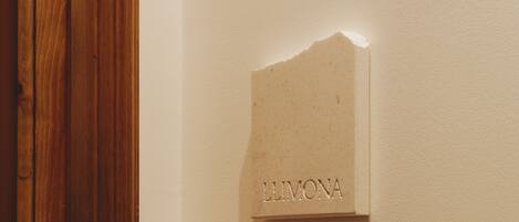 A wooden door adjacent to a wall with a recessed plaque labeled "LLIMONA".