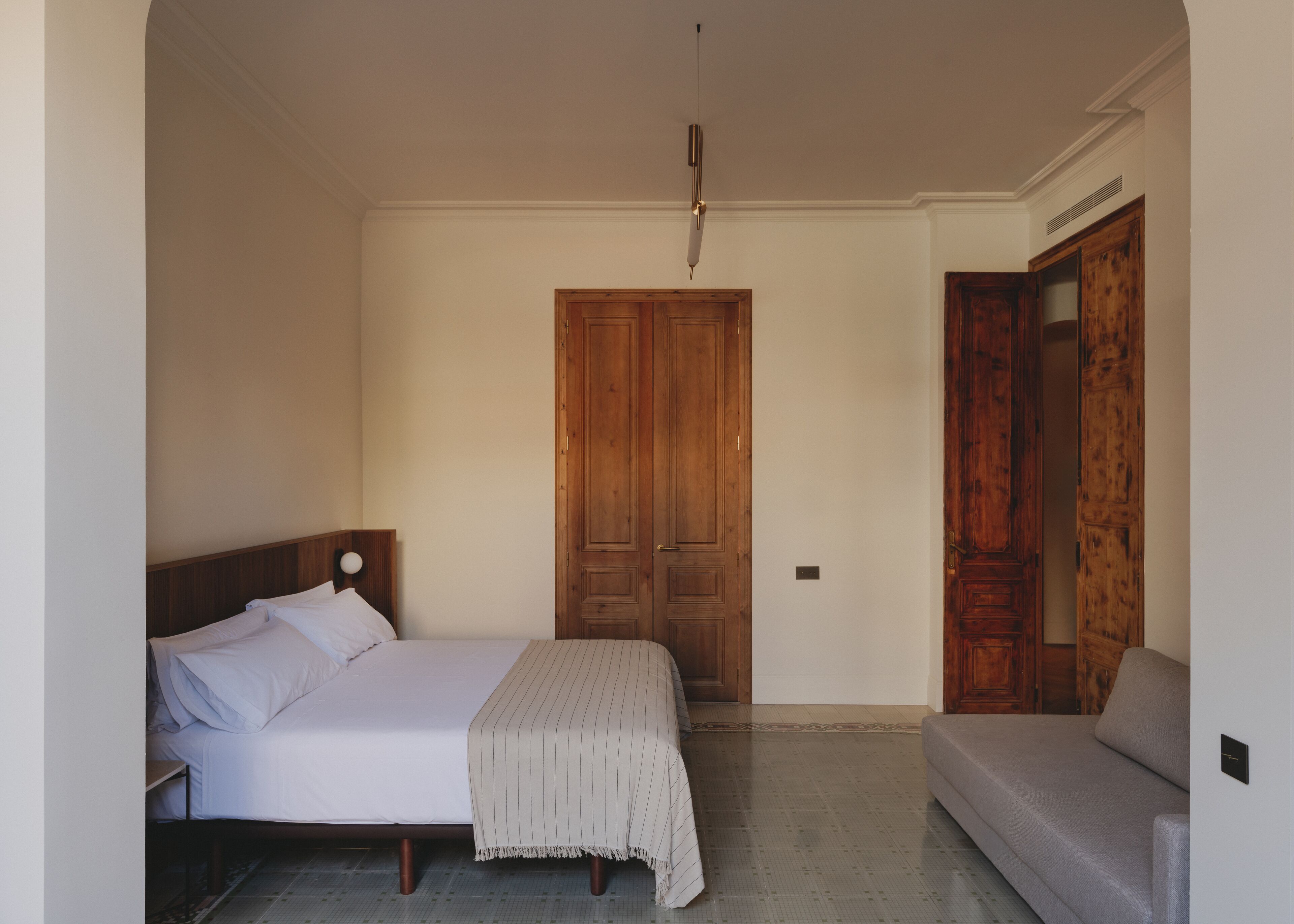 A bedroom with a bed, a bedside table, a wooden wardrobe, and a sofa.
