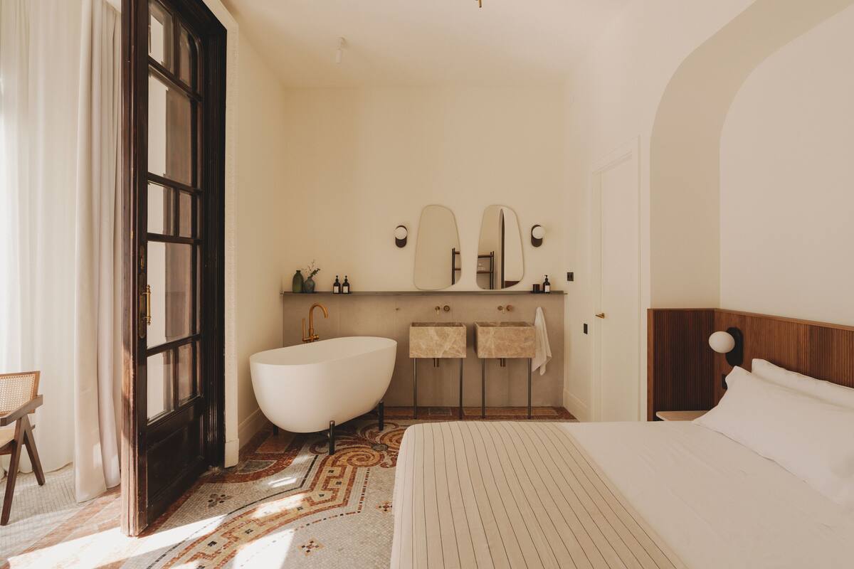 A hotel room with a large bed, a bathtub, a double sink, and a wooden headboard.