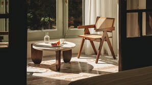 A room with a large window, a wooden chair, a round table with a bottle and a cup, and a patterned rug. - Casa Llimona Hotel Boutique (Barcelona)