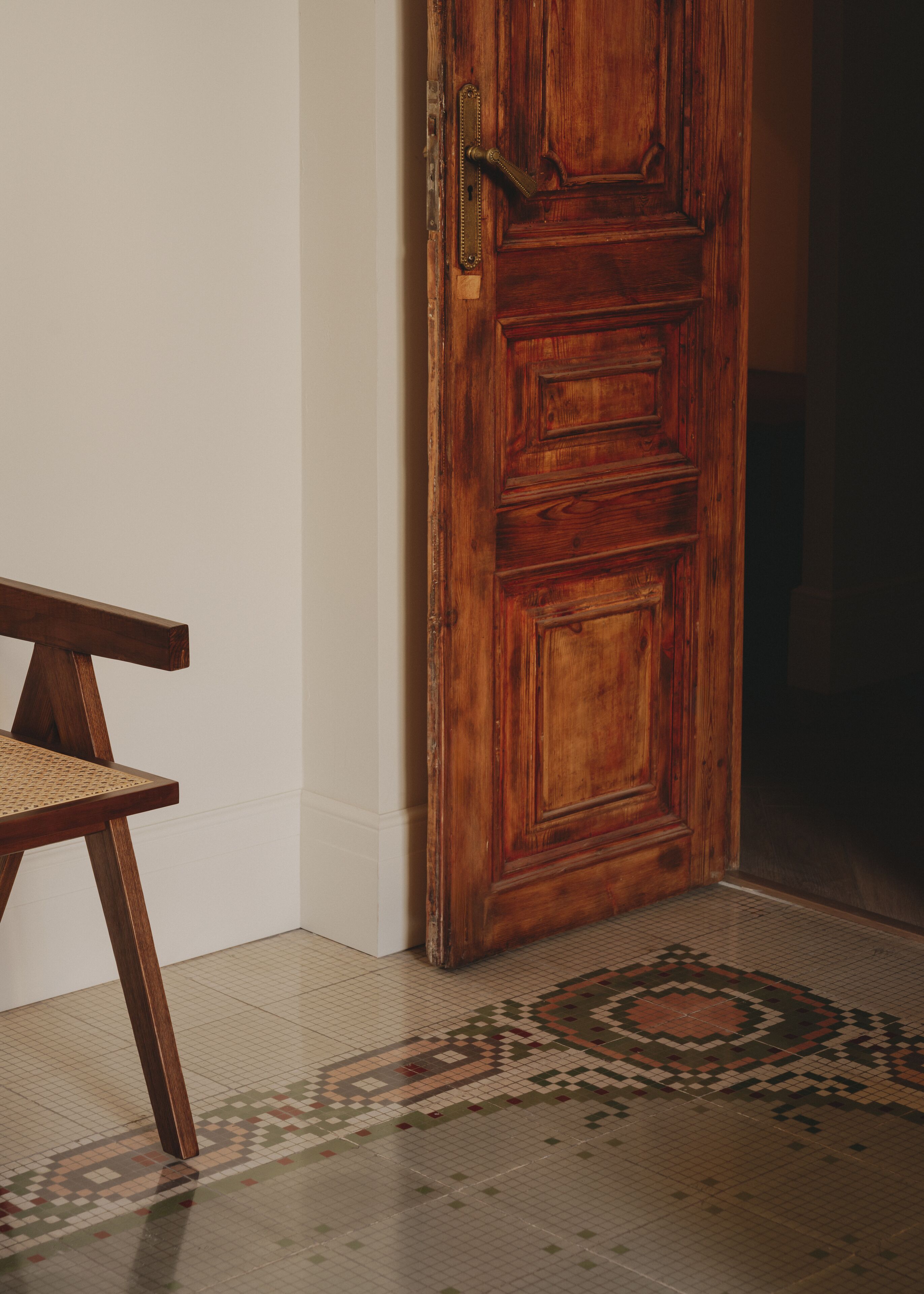 Une porte en bois avec une poignée en laiton, une chaise en osier et un sol à motifs.