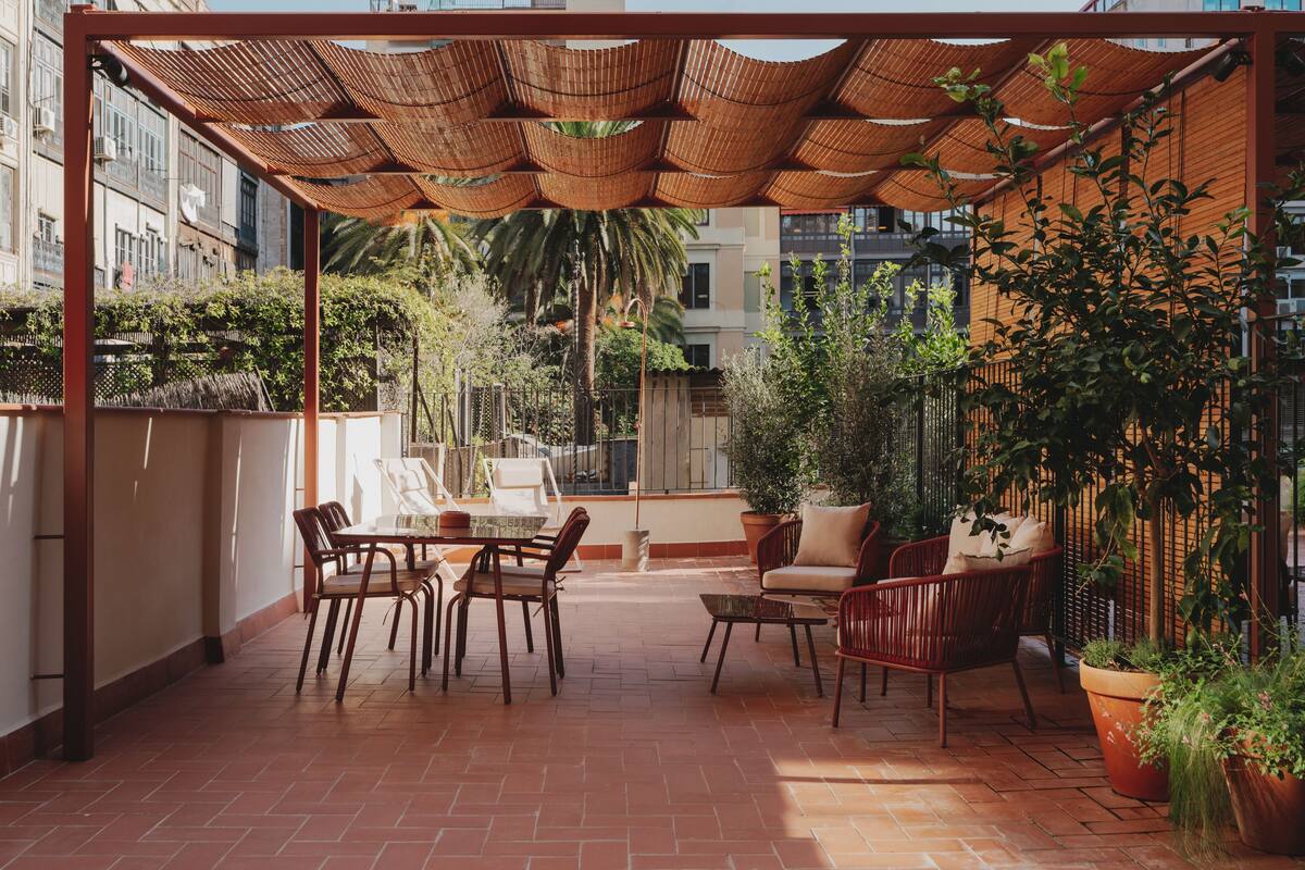 A rooftop patio with a pergola, seating area, and potted plants.