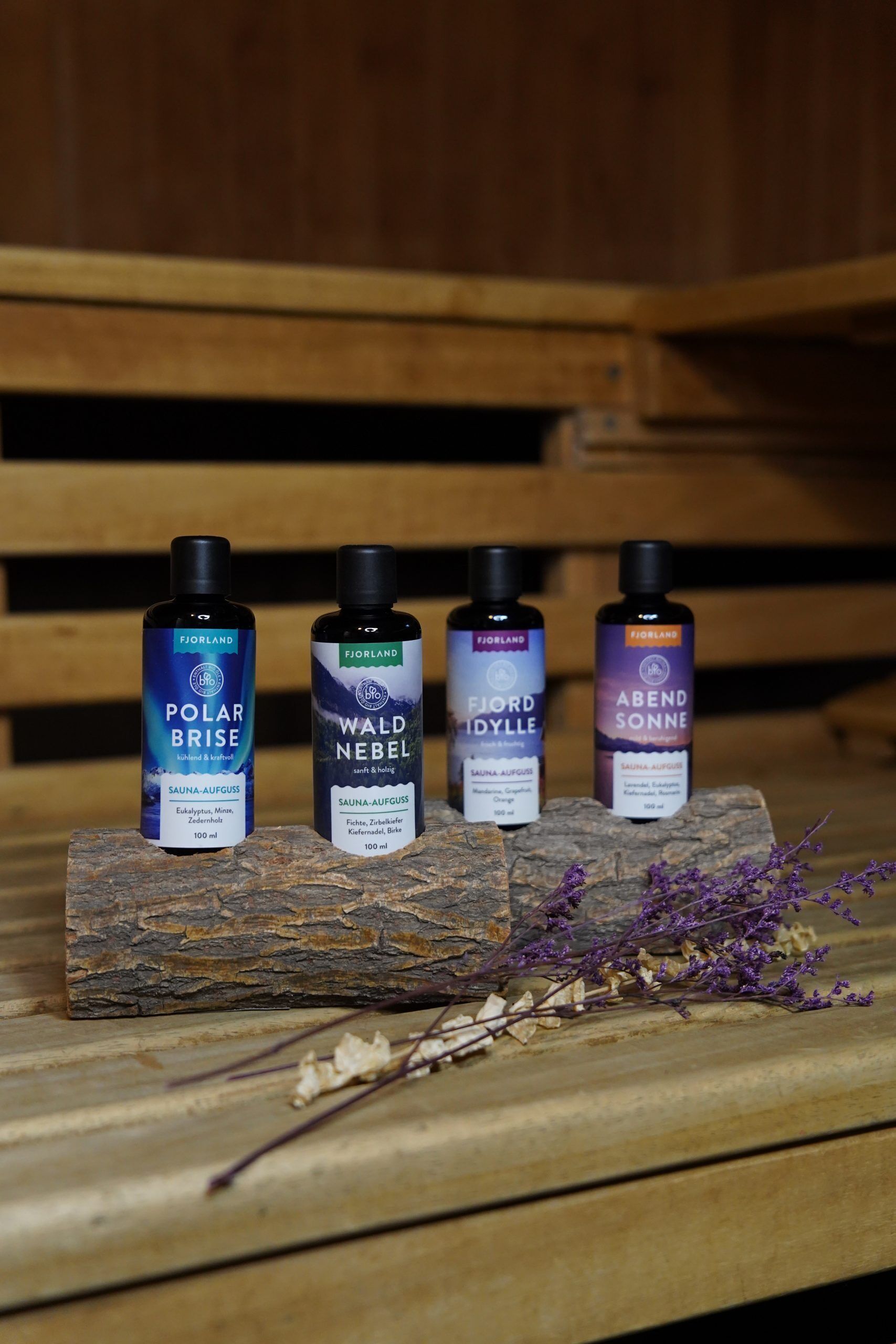 Four bottles of Fjorland sauna products on a wooden surface with dried lavender.