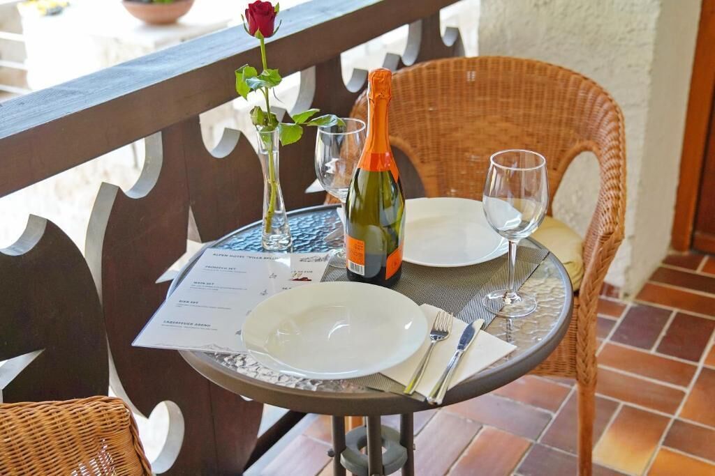 A table set with a bottle of champagne, a rose, and a menu on a balcony with wicker chairs.