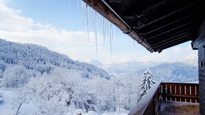 A wooden balcony with a view of snow-covered mountains and trees. - Villa Bello (Berchtesgaden)