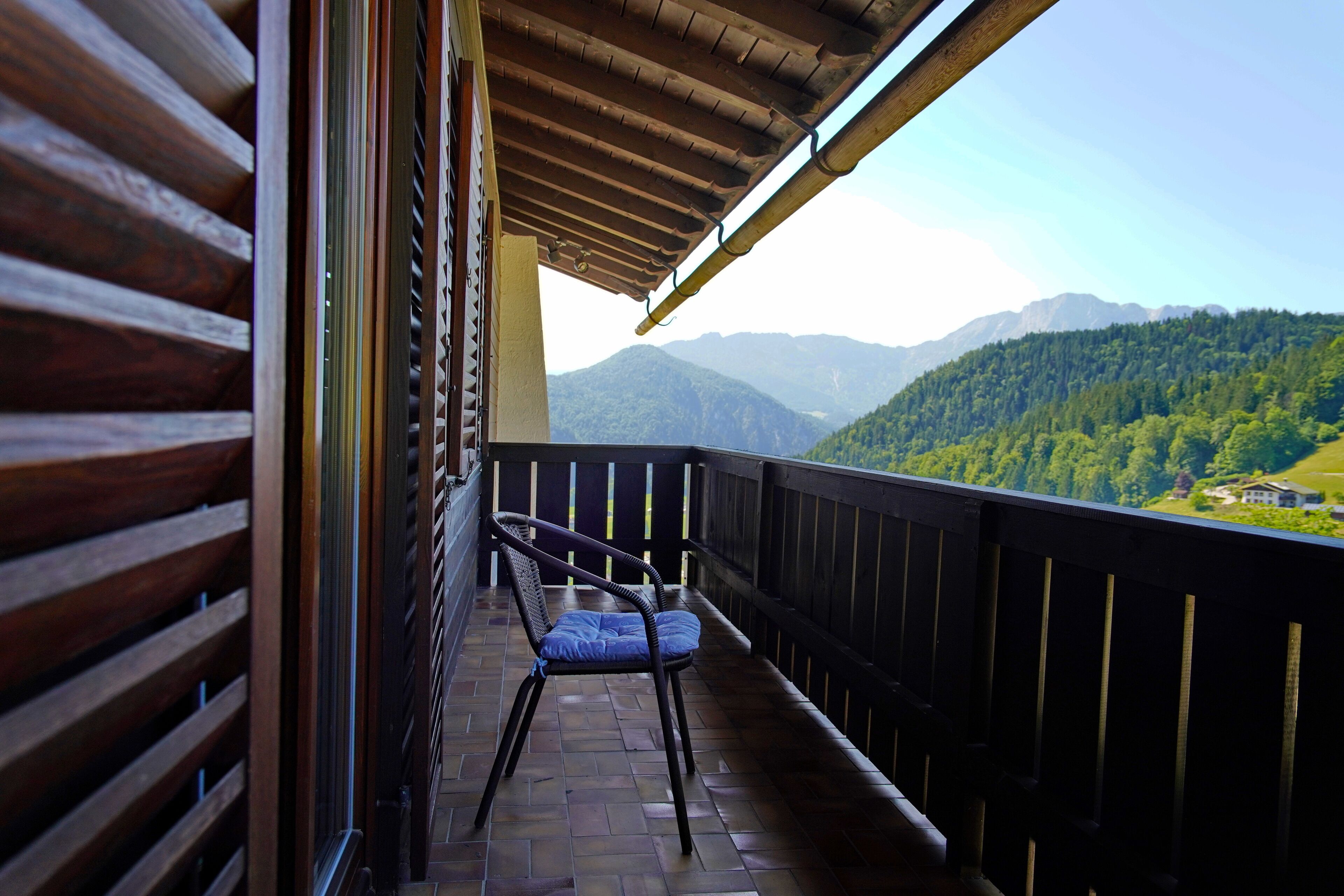 A balcony with a wooden railing, a single chair, and a view of a mountainous landscape.