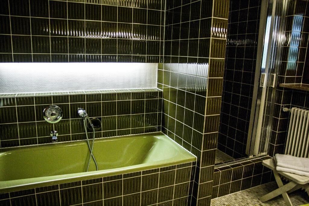 Een badkamer met een groen bad, een douchegedeelte en een witte stoel.