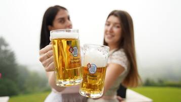 Twee personen met bierglazen met een logo, buiten met een grasveld op de achtergrond.