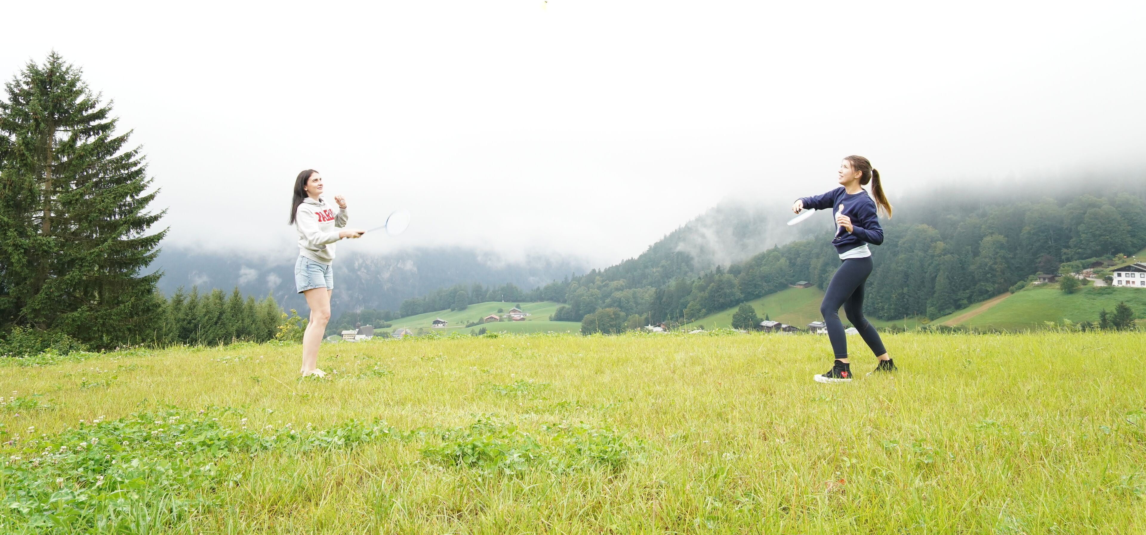 Two people playing with a frisbee on a grassy field with a mountainous backdrop.