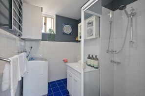 Un baño moderno con una bañera blanca, una ducha con mampara de vidrio y zona de lavamanos con artículos de aseo.