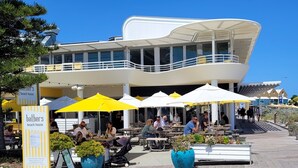 Ein Restaurant am Wasserufer mit Außenbereich, großen Sonnenschirmen und Pflanzkübeln.