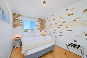 Un dormitorio moderno con una cama, una mesita de noche, un banco y vistas a la ciudad.