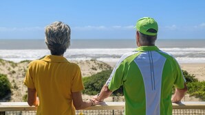 Due persone che guardano una spiaggia con onde e sabbia.