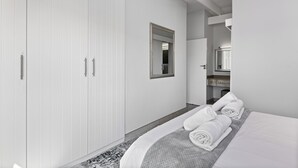 Camera d'albergo moderna con un ampio guardaroba, un letto con asciugamani ordinatamente piegati e un bagno piccolo con uno specchio e un lavandino.